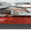Dettaglio di quadro astratto con elementi a rilievo e inserti metallici su sfondo grigio e rosso
