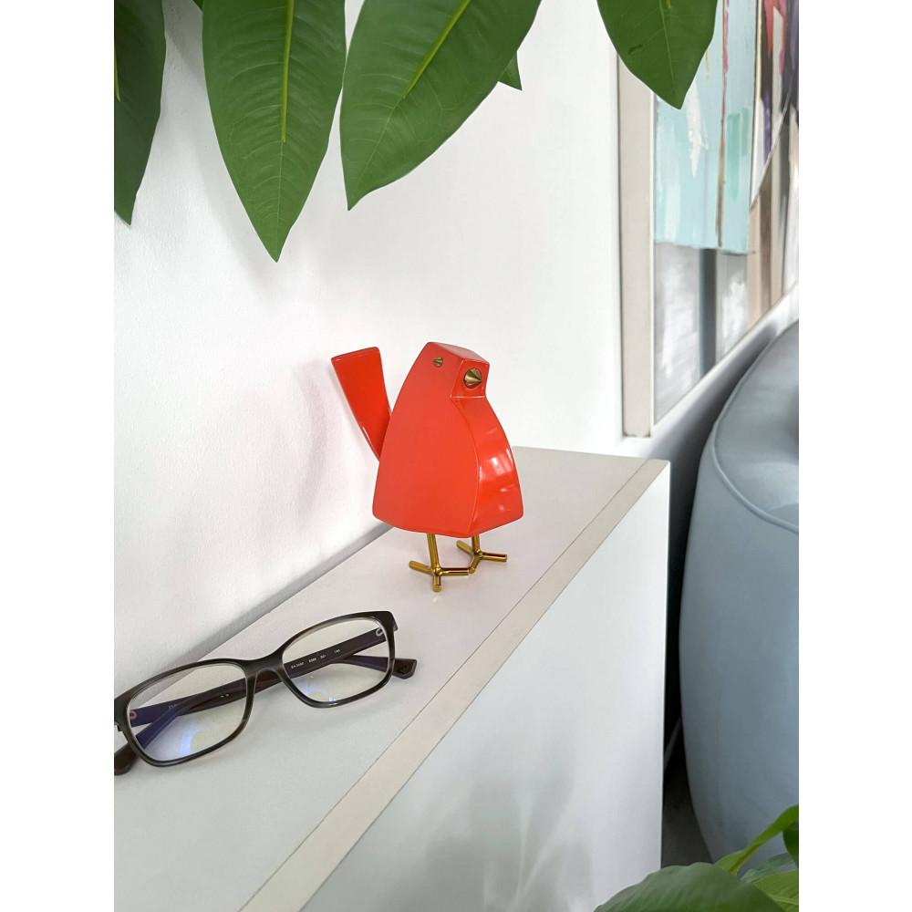 Uccellino in resina arancione posizionato su un ripiano in legno con caffettiera