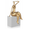 statuetta effetto oro che raffigura una donna con le gambe accavallate e un braccio dietro la testa