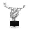 Statua di colore grigio chiaro metallizzato che si chiama Equilibrio che rappresenta una figura umana maschile accovacciata su un piedistallo