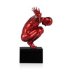 Statua rosso metallizzato di un uomo in equilibrio su un piedistallo visto di profilo